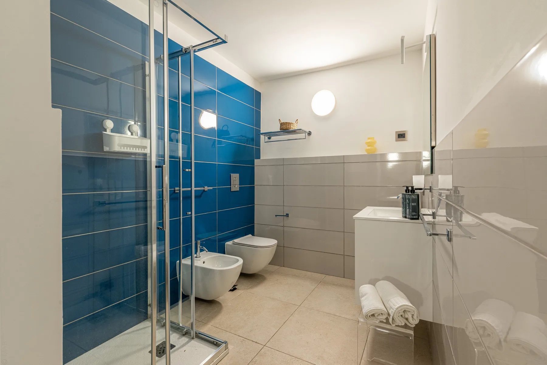 Un baño moderno con ducha de vidrio, lavabo mural e inodoro.
