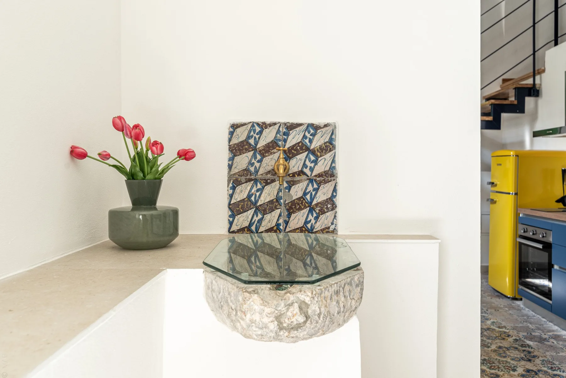 Un interior luminoso con una mesa de vidrio, flores en maceta y arte mural estampado.