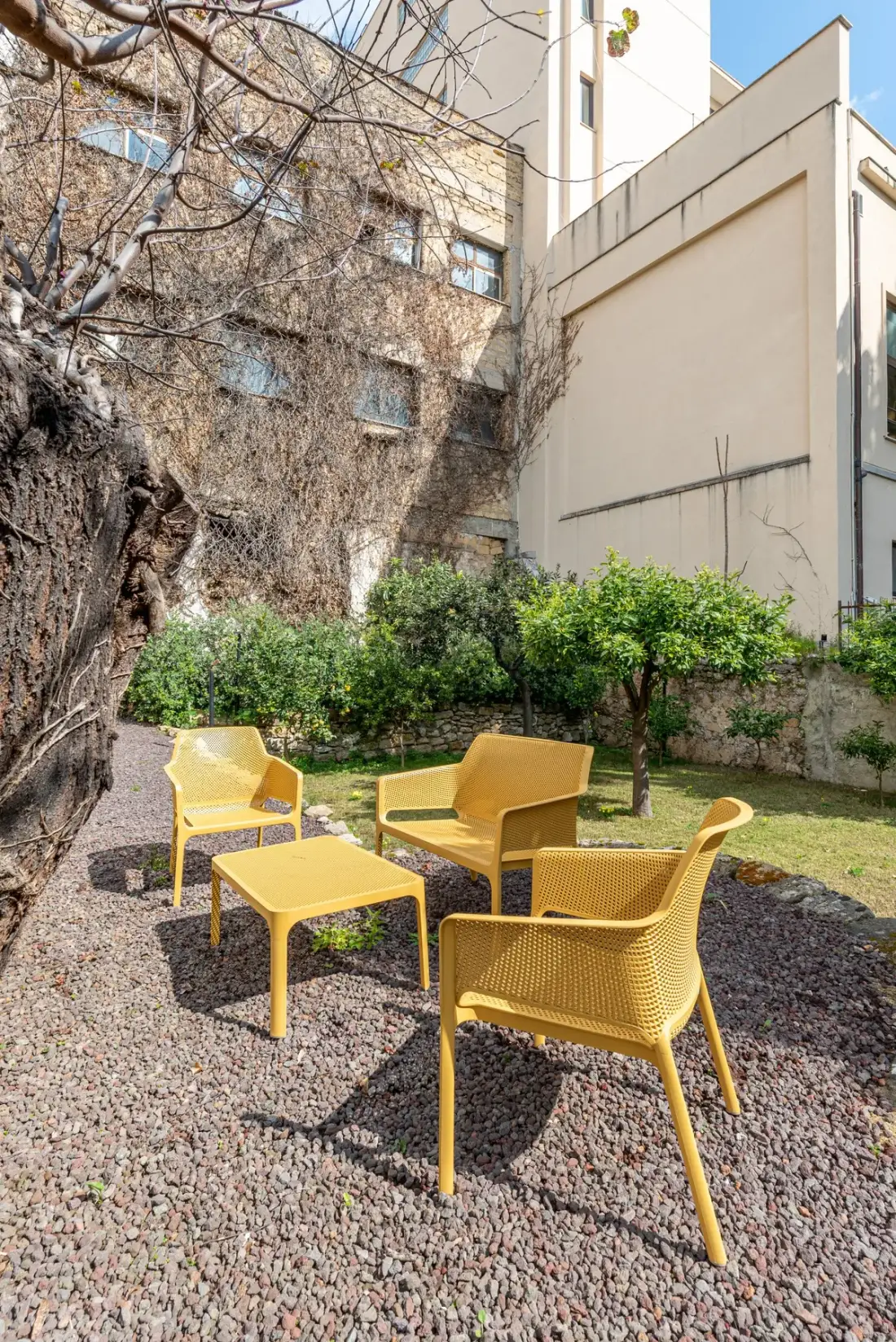 Una zona de estar al aire libre con sillas amarillas y una mesa junto a un jardín.