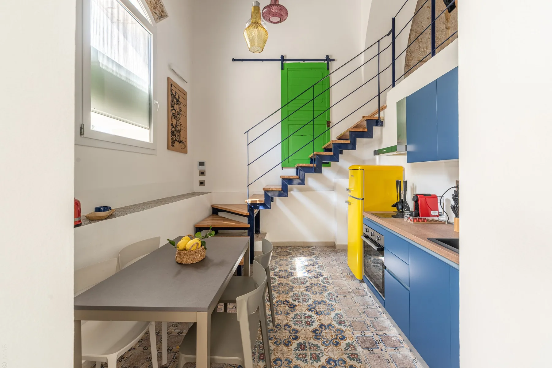 Una cocina y comedor luminosos con armarios azules y una escalera.