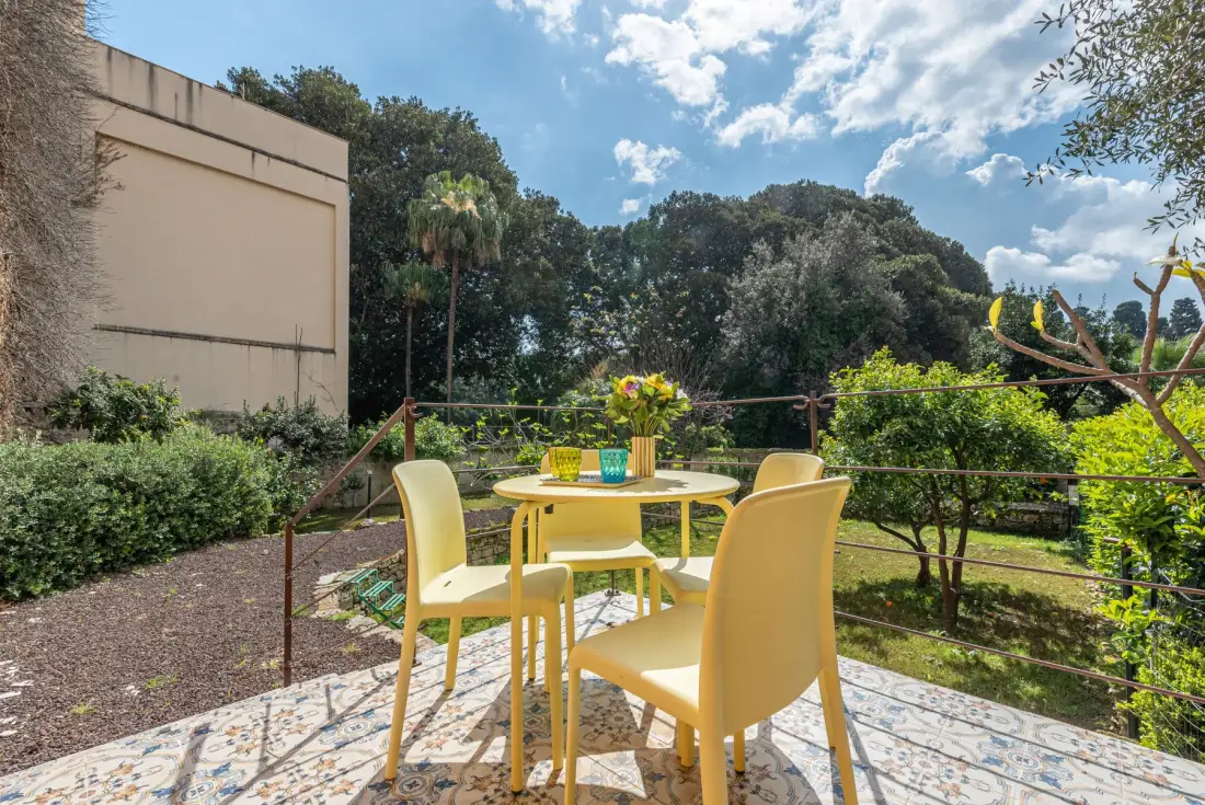 Un comedor al aire libre con una mesa redonda y asientos amarillos da a una zona verde.