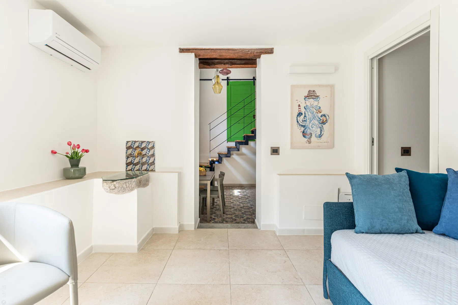 Una habitación luminosa con asientos azules y una puerta abierta hacia una escalera.