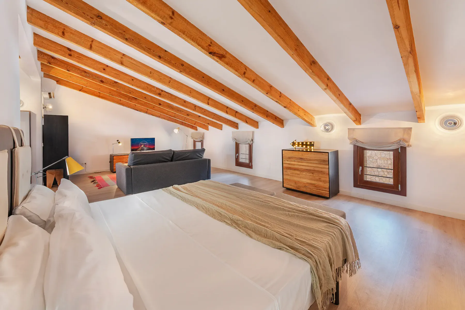 A bright bedroom with a large bed and exposed wooden ceiling beams.