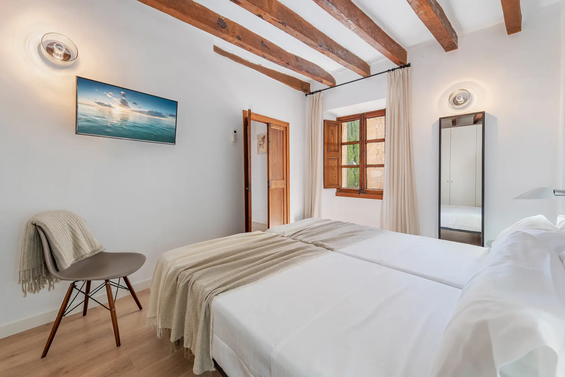 A bright bedroom with white bedding, exposed ceiling beams, and a wooden window.