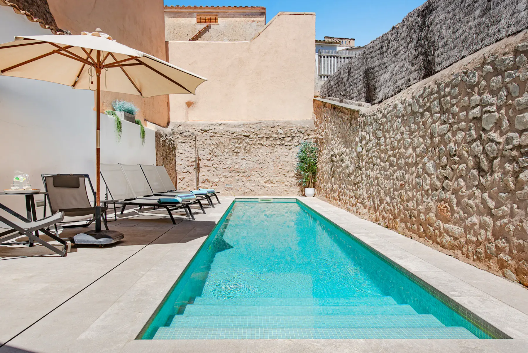 A small outdoor swimming pool is surrounded by stone walls and lounge seating.