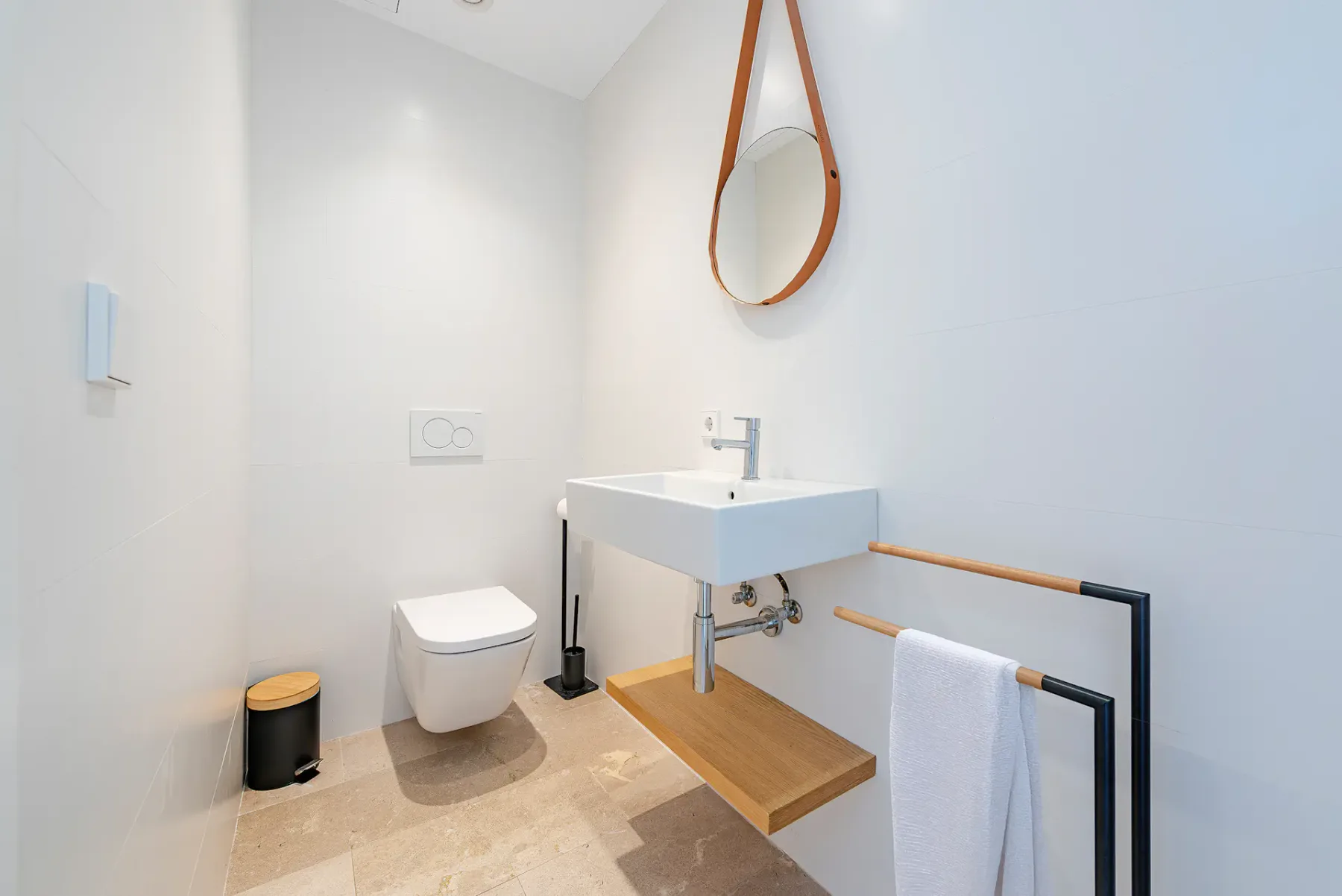 A bright bathroom with a wall-mounted sink, toilet, and round mirror.