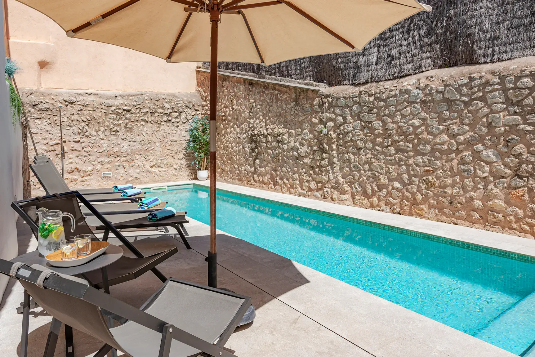 An outdoor swimming pool is bordered by lounge seating and a large umbrella.