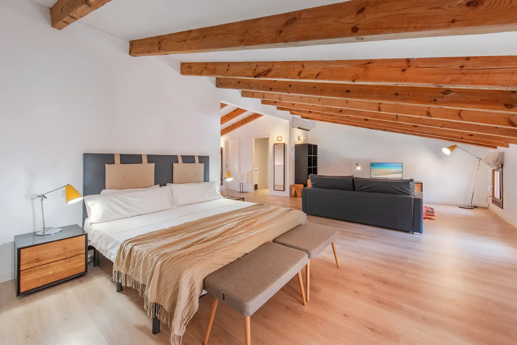 A spacious bedroom with a large bed, exposed wooden ceiling beams, and a seating area.