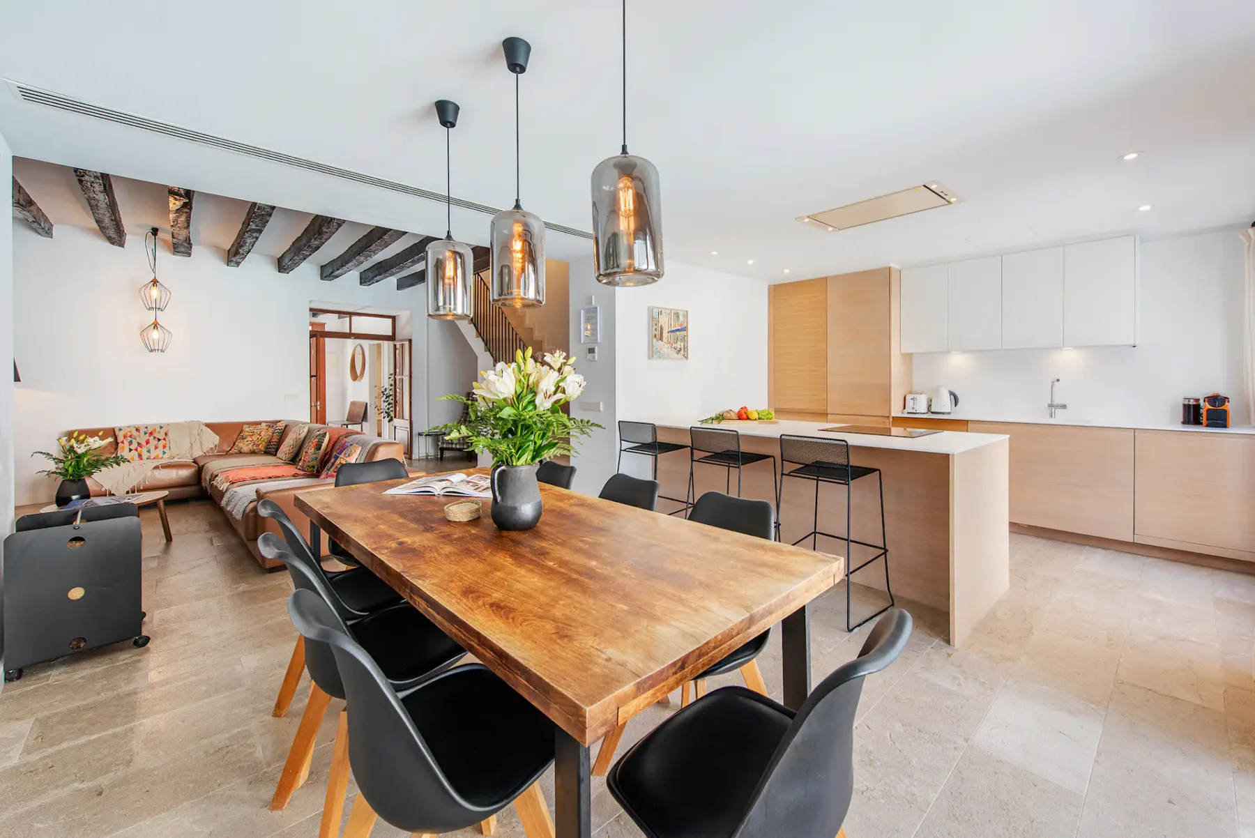 A dining area with a long wooden table opens onto a bright kitchen.