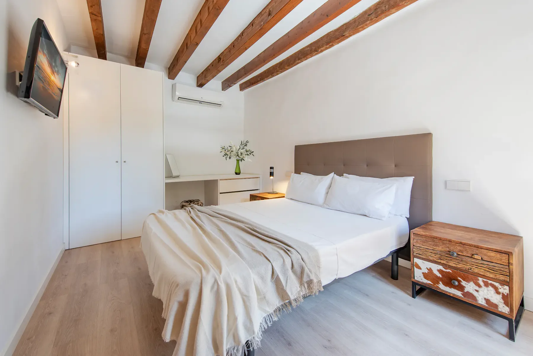 A bedroom with a double bed, white wardrobe, and exposed wooden ceiling beams.
