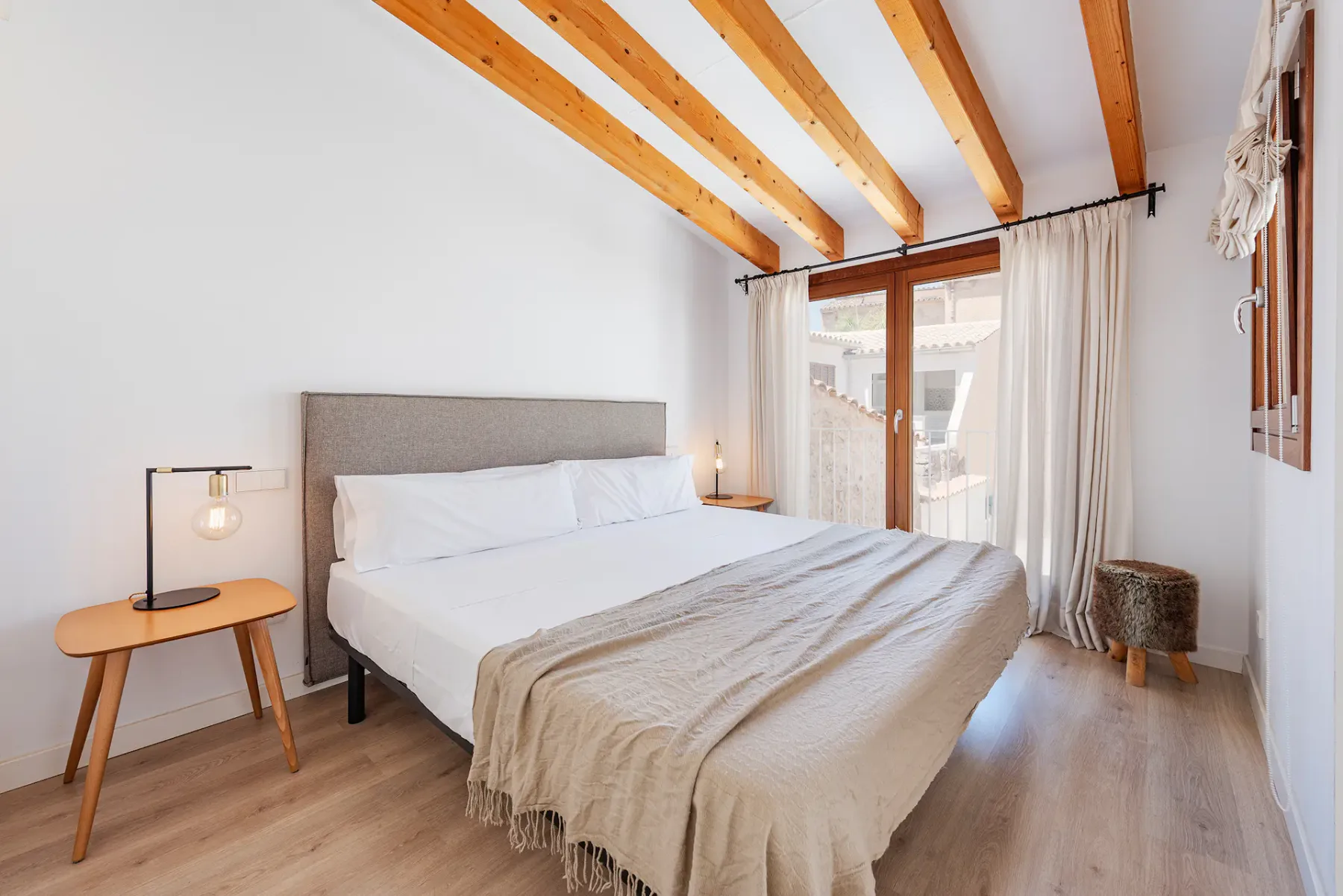 A bright bedroom with a large bed and exposed wooden ceiling beams.