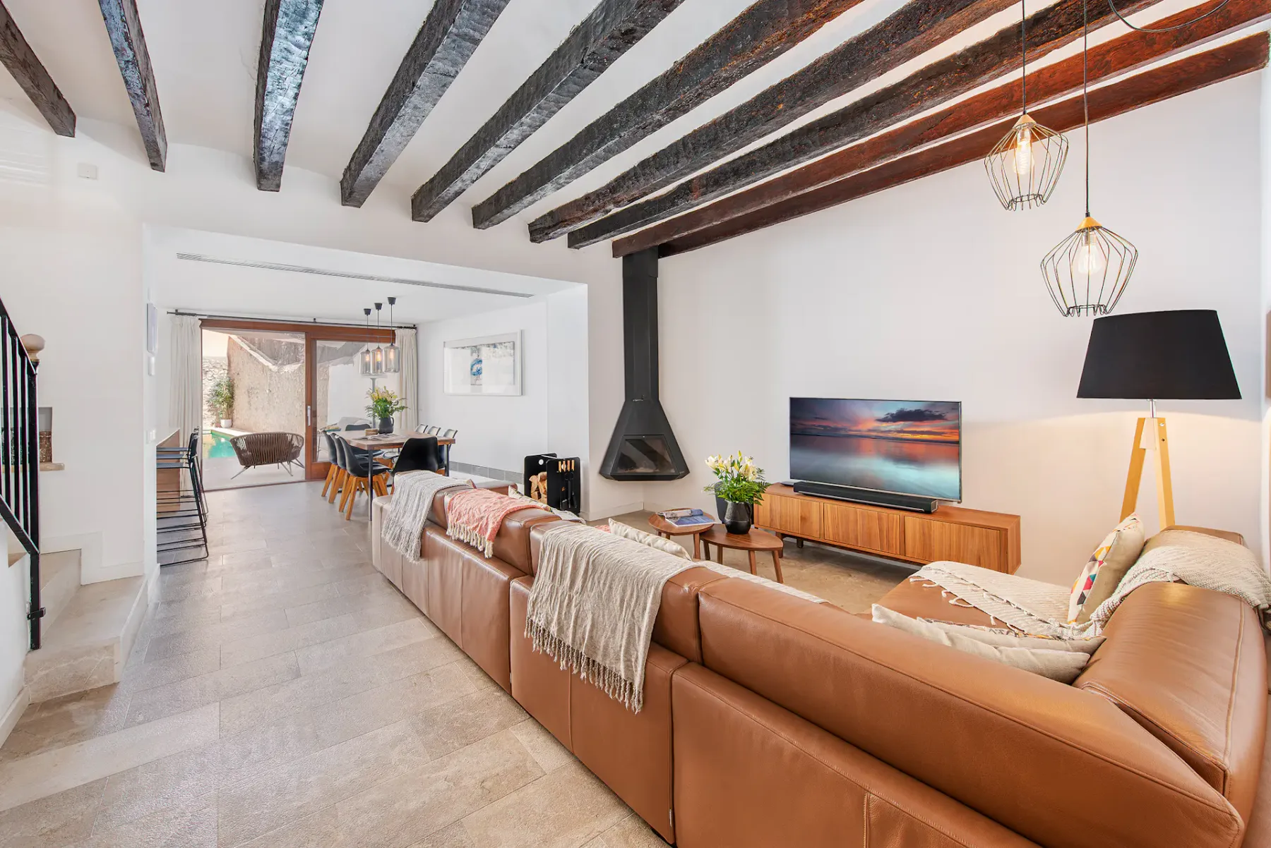 A bright living room with leather seating, a television, and exposed ceiling beams.