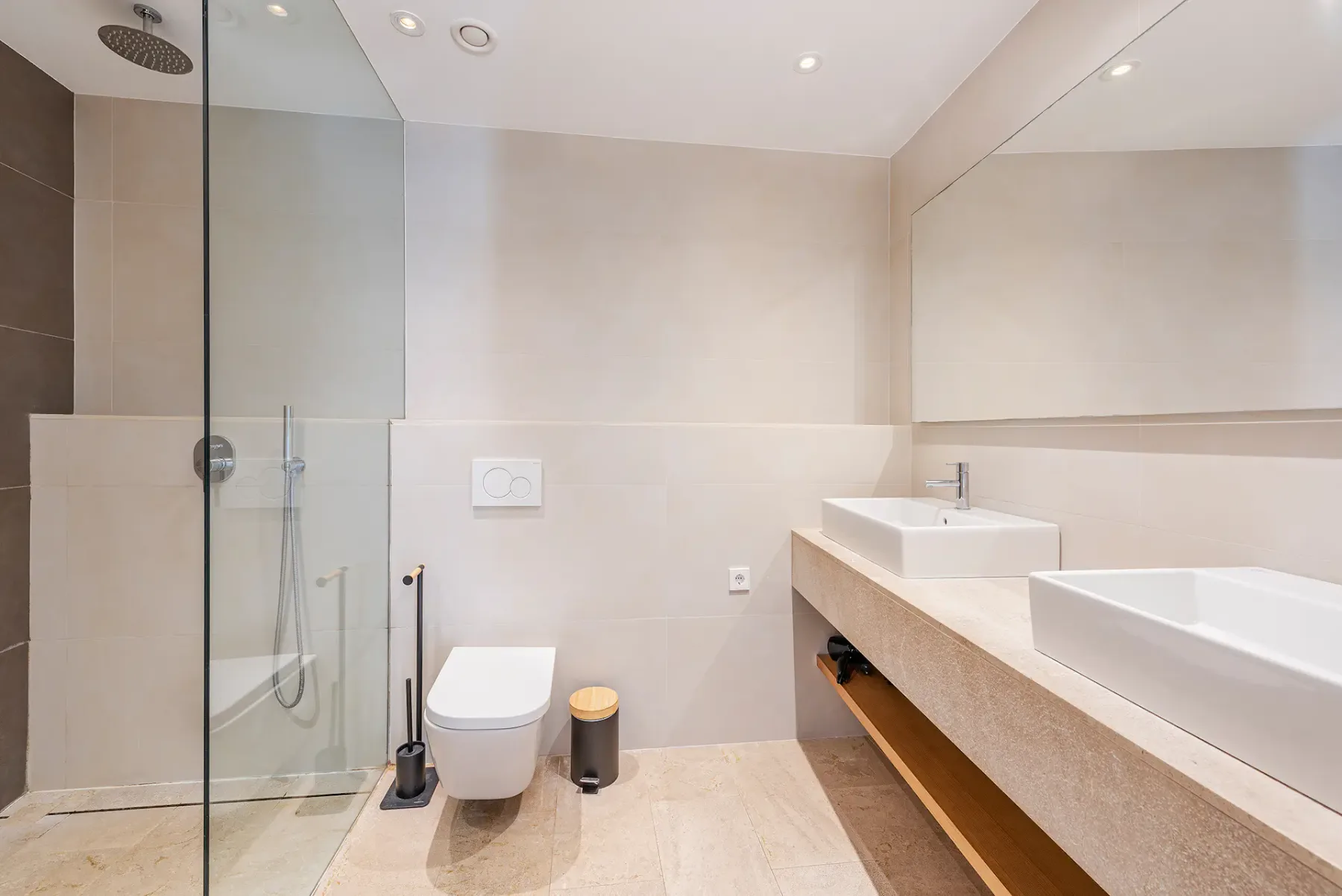 A bright bathroom with a glass shower and a long vanity.