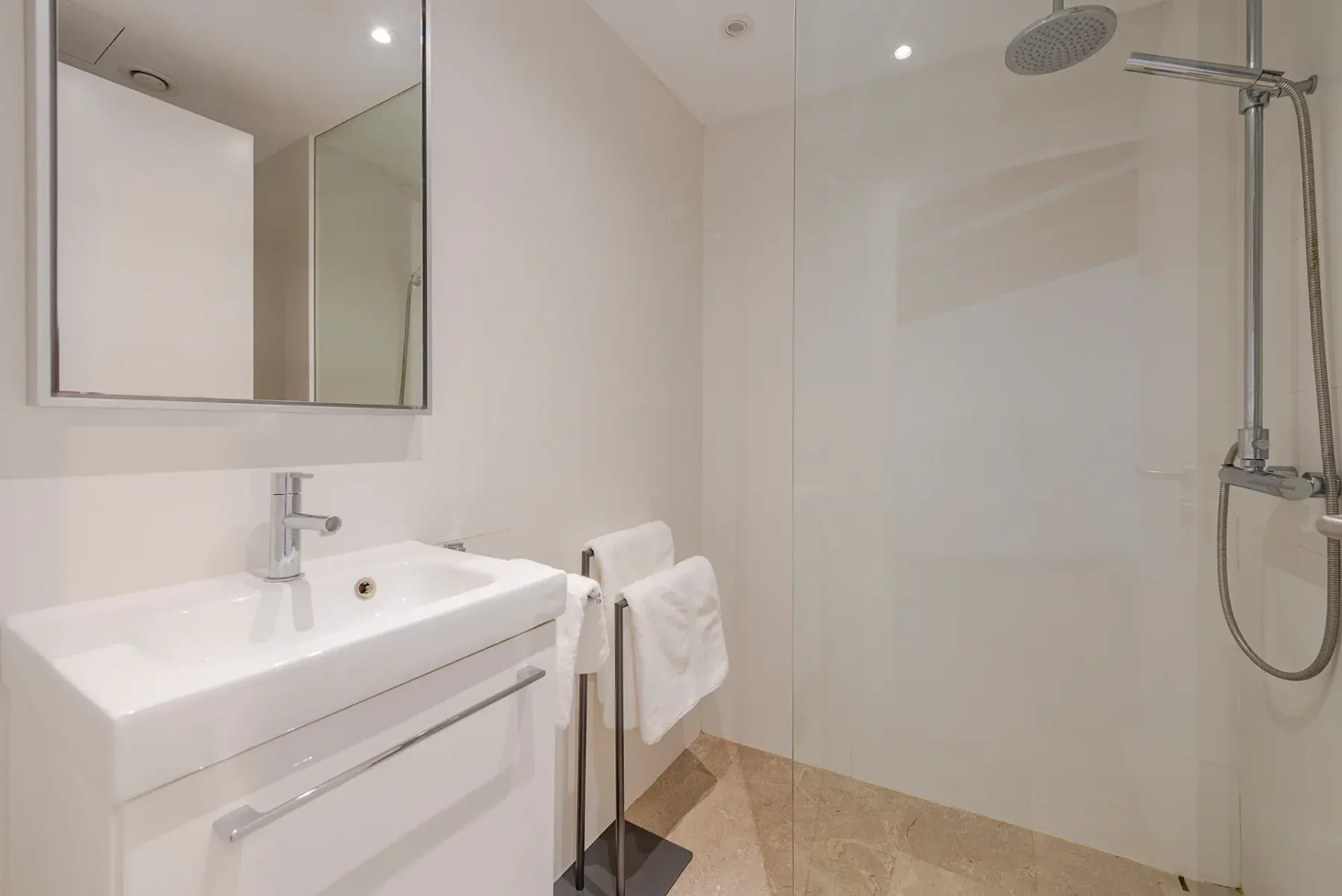 A bright bathroom with a sink, mirror, and walk-in shower.