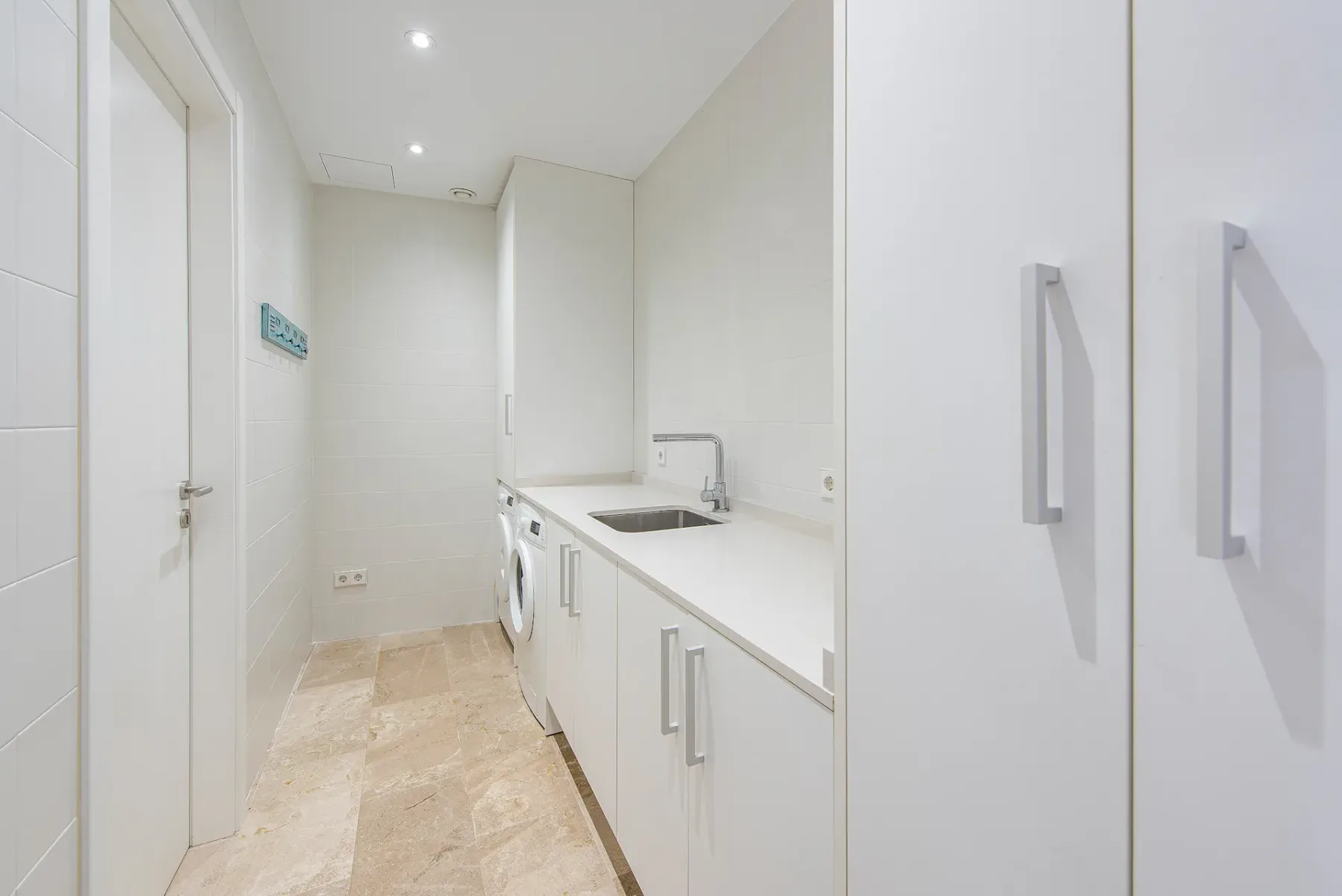 A bright utility room with a washing machine beneath a white countertop.