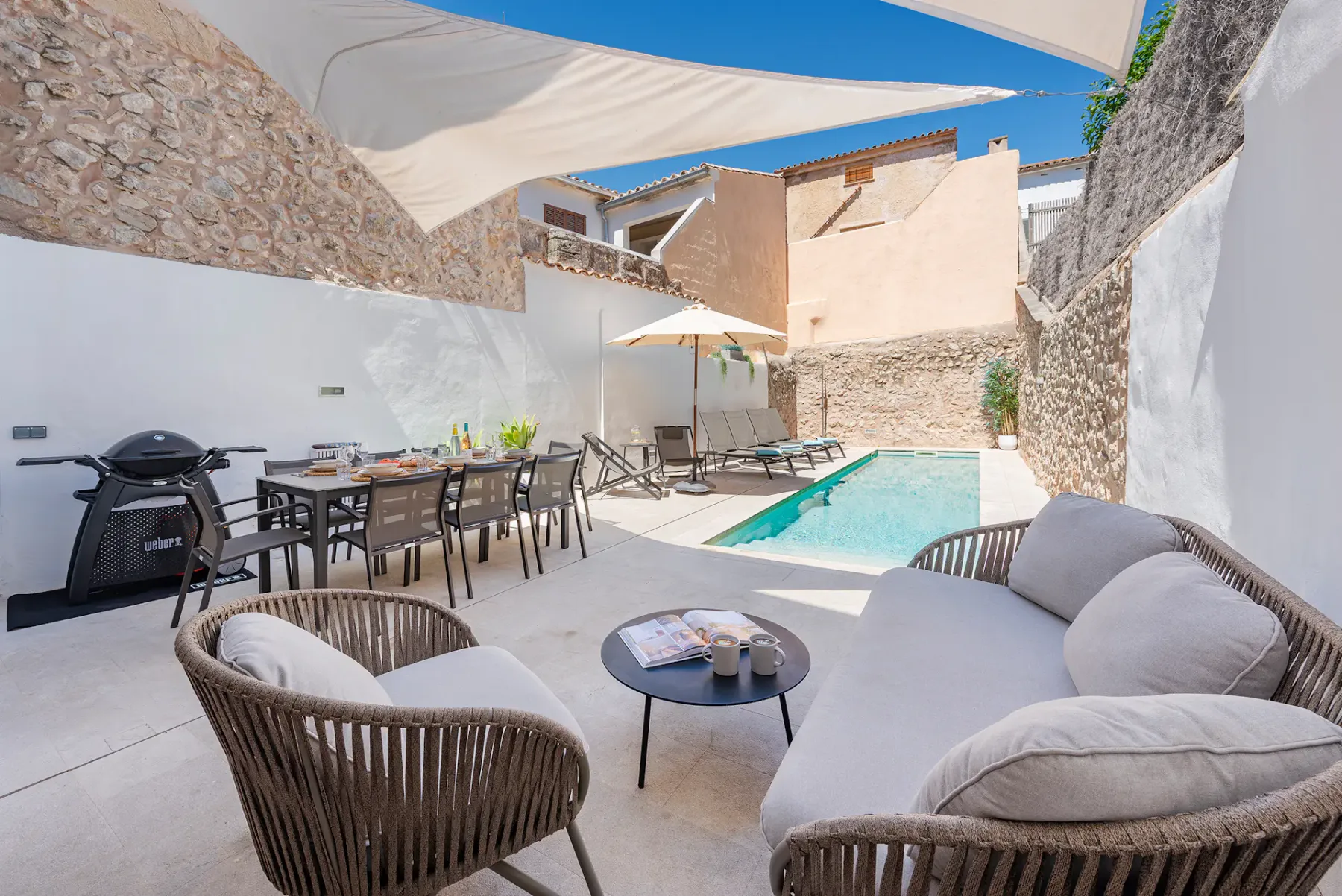 A sunlit courtyard patio has outdoor seating, a dining table, and a swimming pool.
