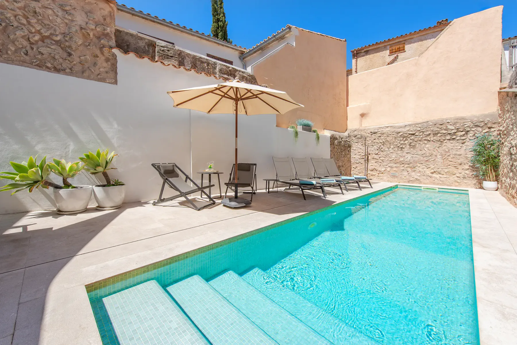 A sunny outdoor pool patio with lounge seating and a large umbrella.
