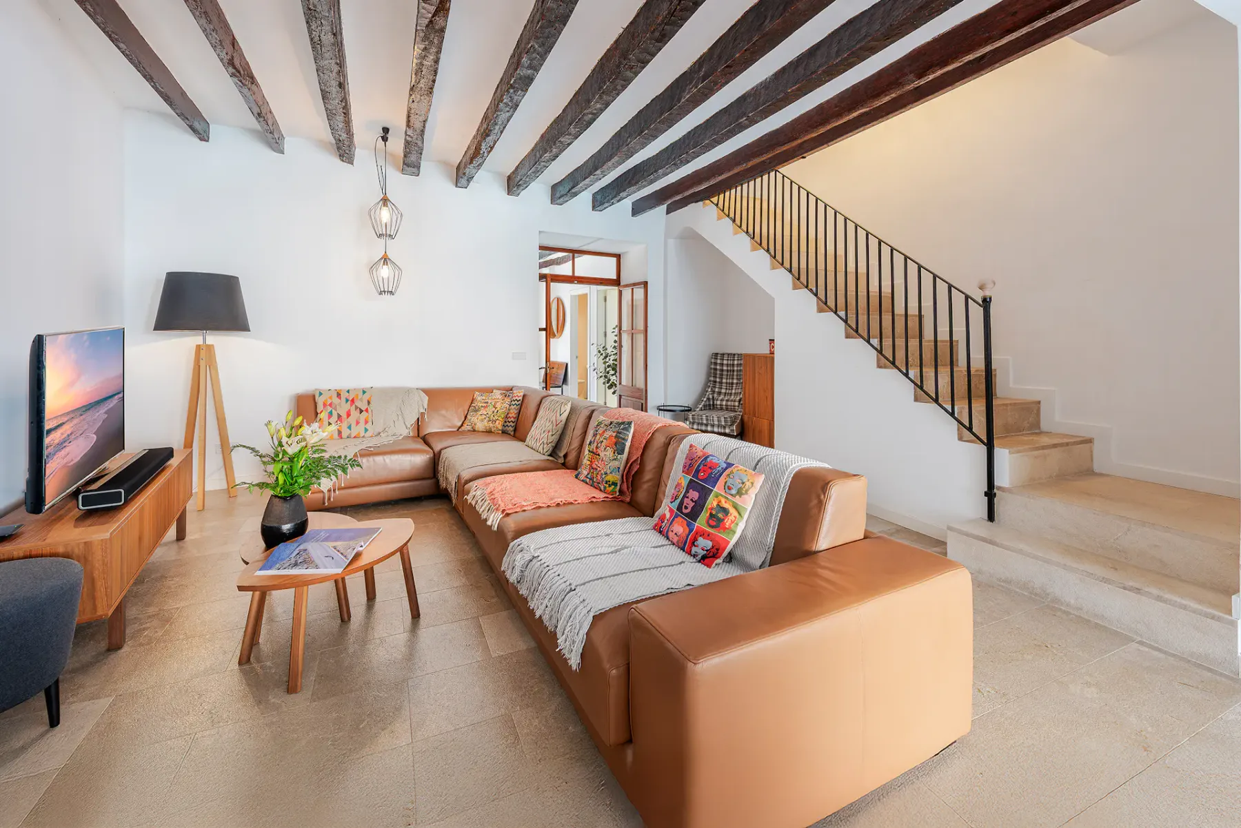 A living room with sectional seating, a television, and a staircase.