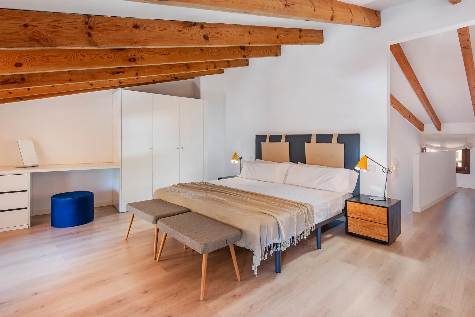 A bedroom with a bed, bedside tables, and exposed wooden ceiling beams.