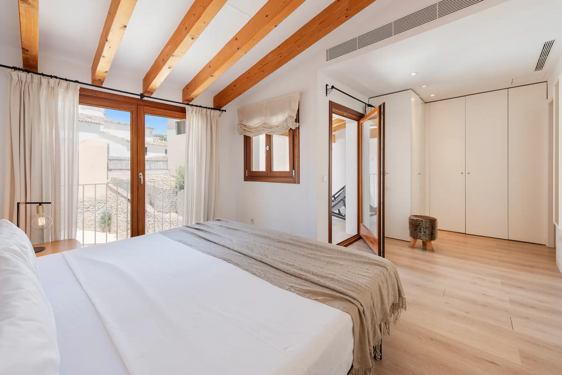 A bright bedroom with a neatly made bed and large glass doors.