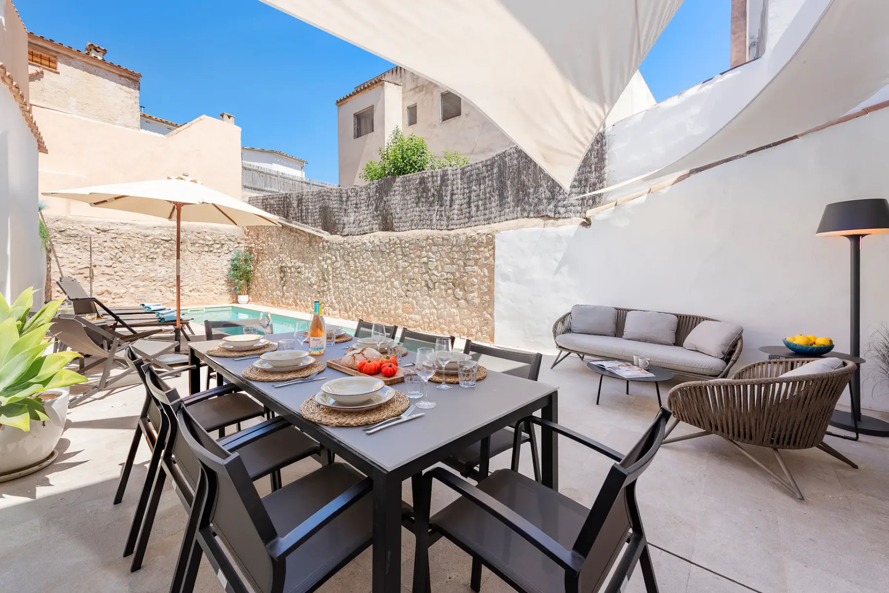 A sunlit outdoor dining terrace with a table, seating, and a stone wall.