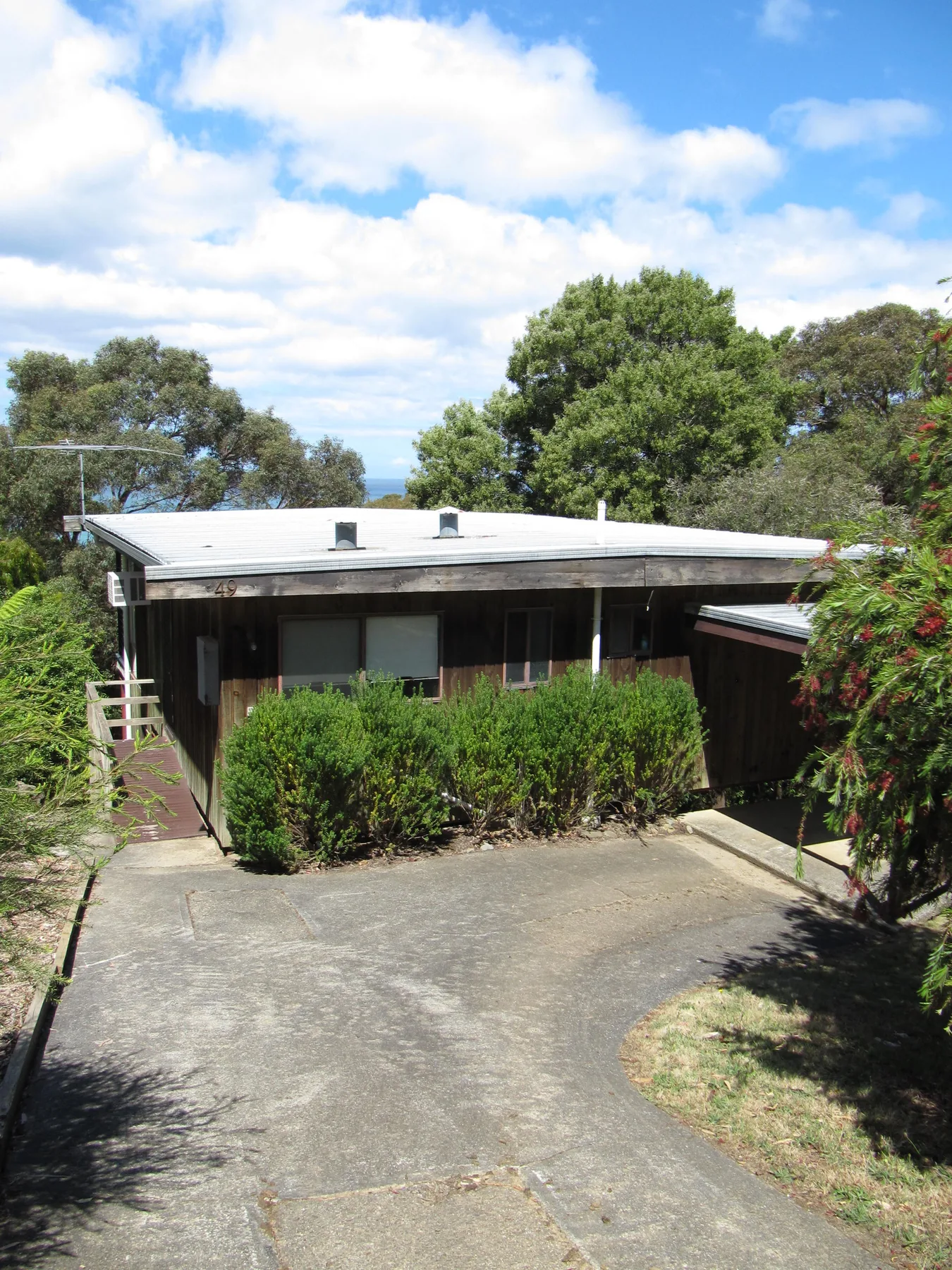 A low, single-story building stands behind a paved driveway and shrubs.