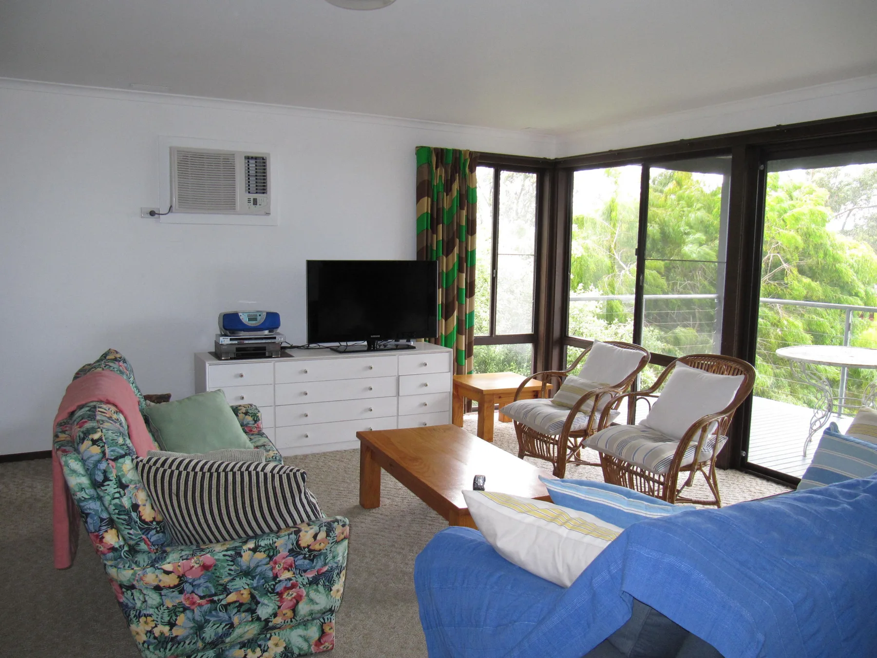 A bright living room has seating around a wooden coffee table beside large windows.