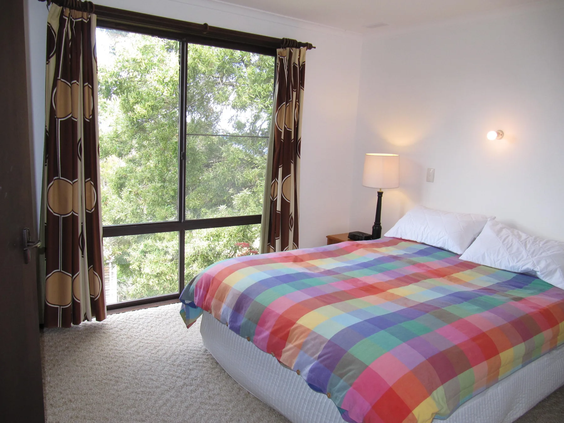 A bright bedroom with a large bed beside a floor-to-ceiling window.