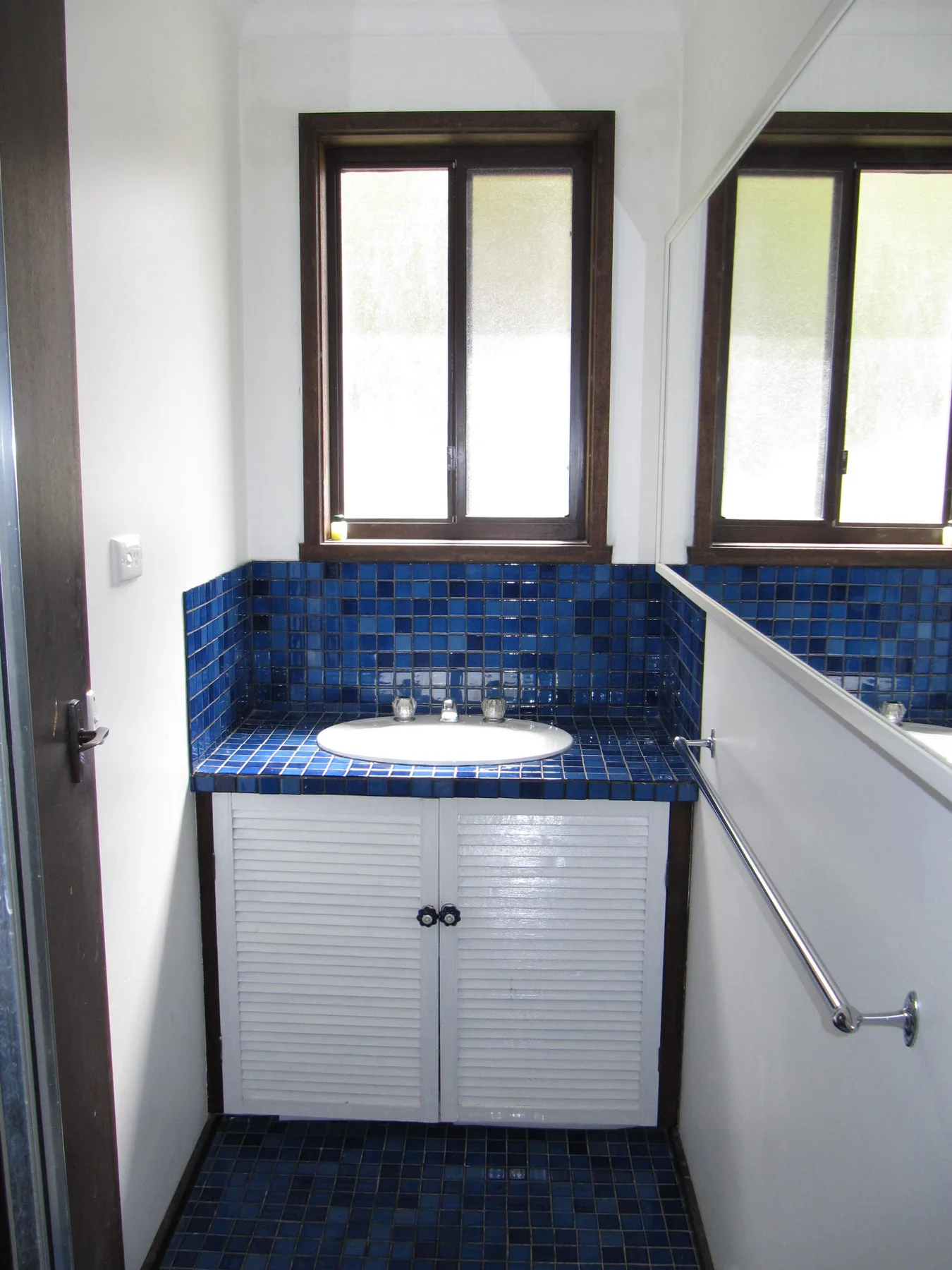 A compact bathroom vanity with a white sink and blue tiled surfaces.