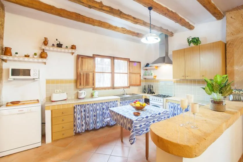 A kitchen and dining area with wooden ceiling beams and a tiled tablecloth.