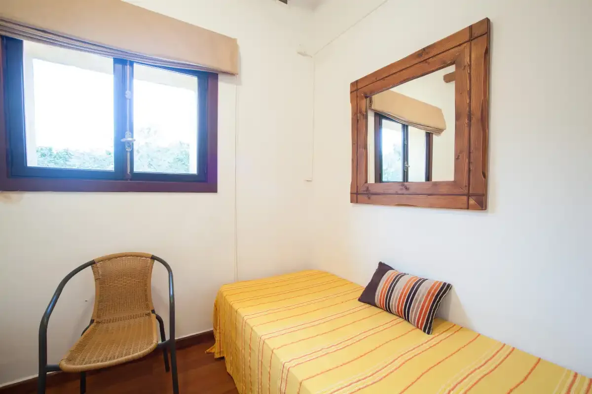 A bedroom with a single bed, a chair, and a window.