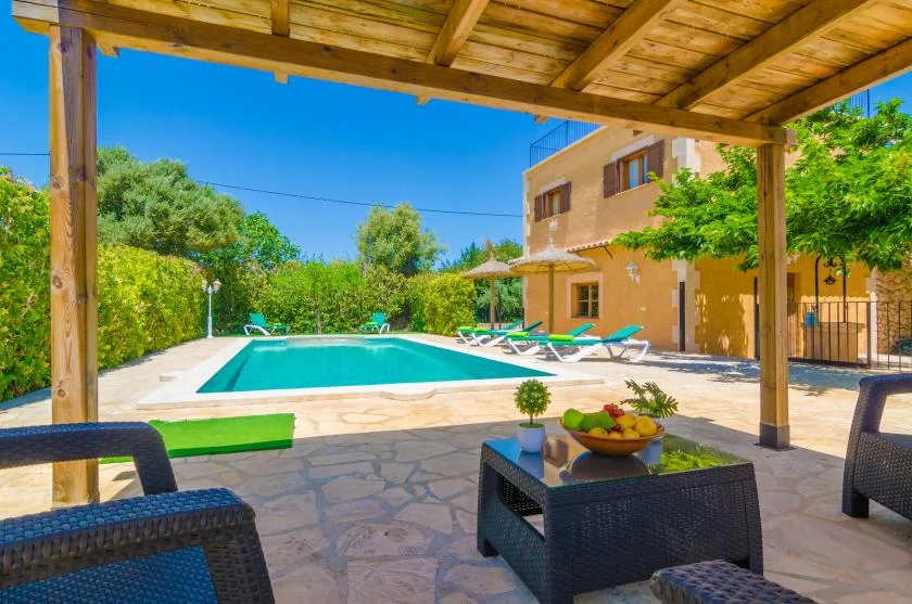 A shaded patio overlooks a swimming pool beside a sunlit house.
