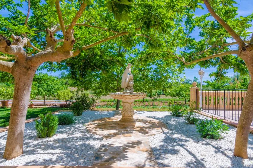 A shaded garden courtyard with a stone fountain beneath leafy trees.