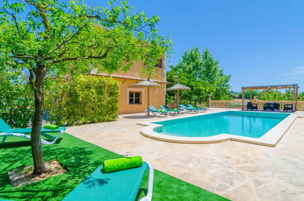 An outdoor swimming pool beside a house, with lounge seating and trees.