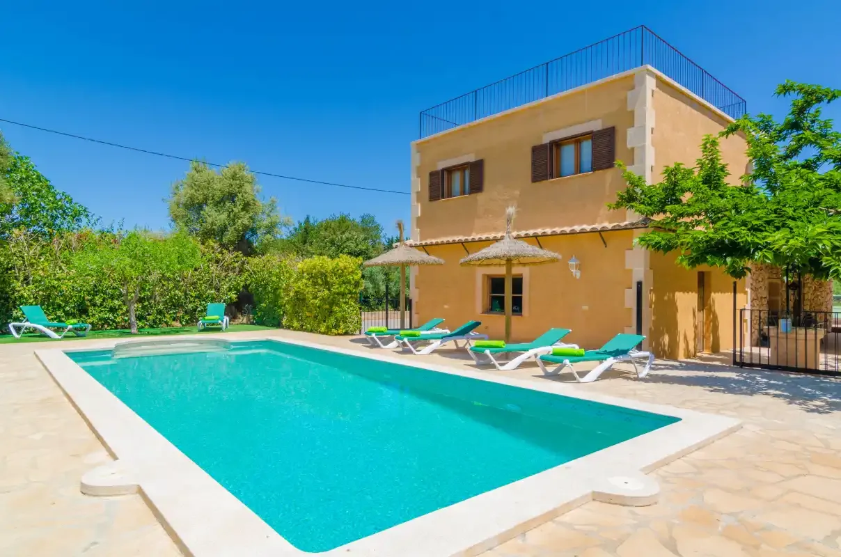 A swimming pool beside a tan two-story house and sun loungers.