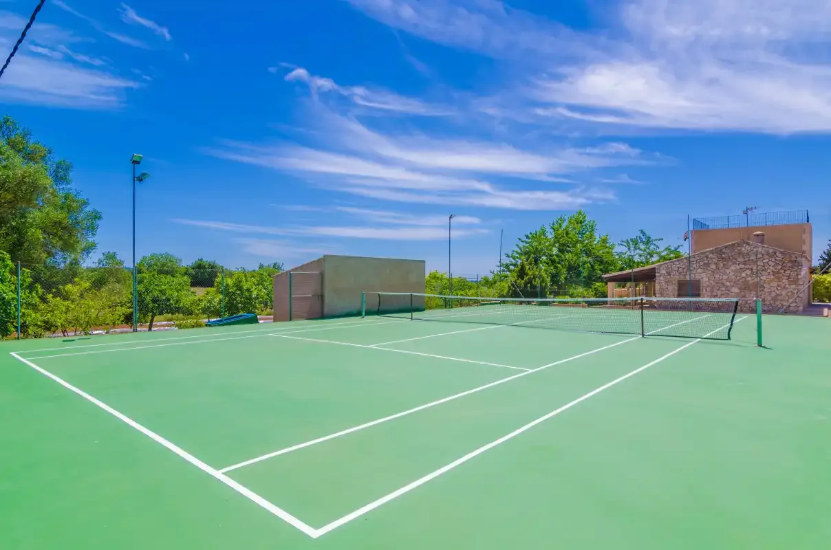 An outdoor tennis court with a net and trees beneath a blue sky.
