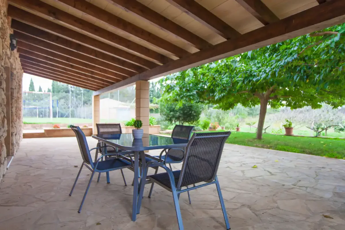 A covered patio has a dining table and seating overlooking a green garden.