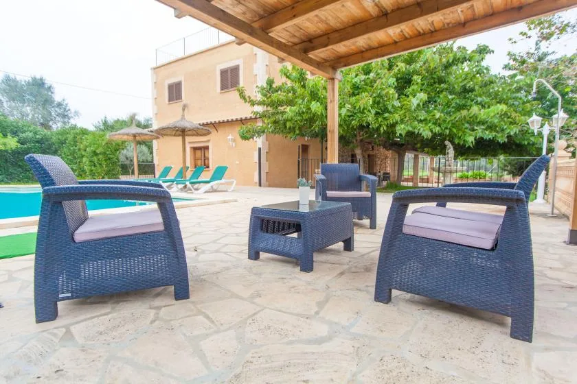 A stone patio with outdoor seating sits beside a pool and a leafy tree.