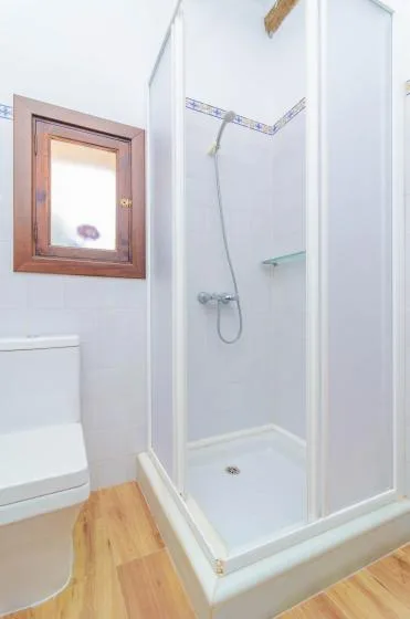 A tiled bathroom with a glass shower and a small wooden-framed window.