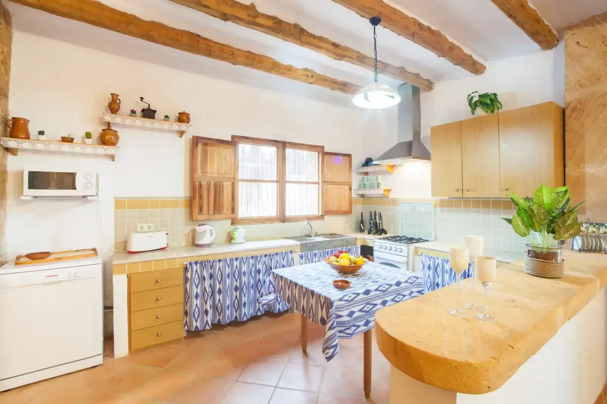 A rustic kitchen with wooden ceiling beams, a tiled work area, and a dining table.