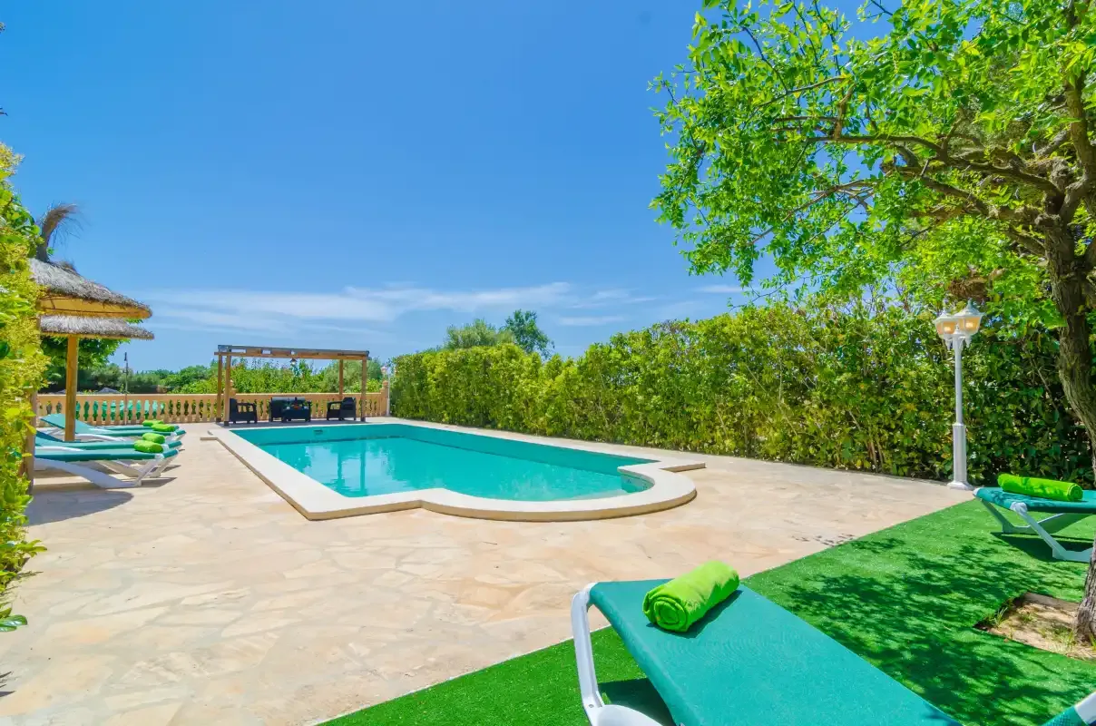 An outdoor swimming pool sits beside a paved patio with lounge seating and greenery.