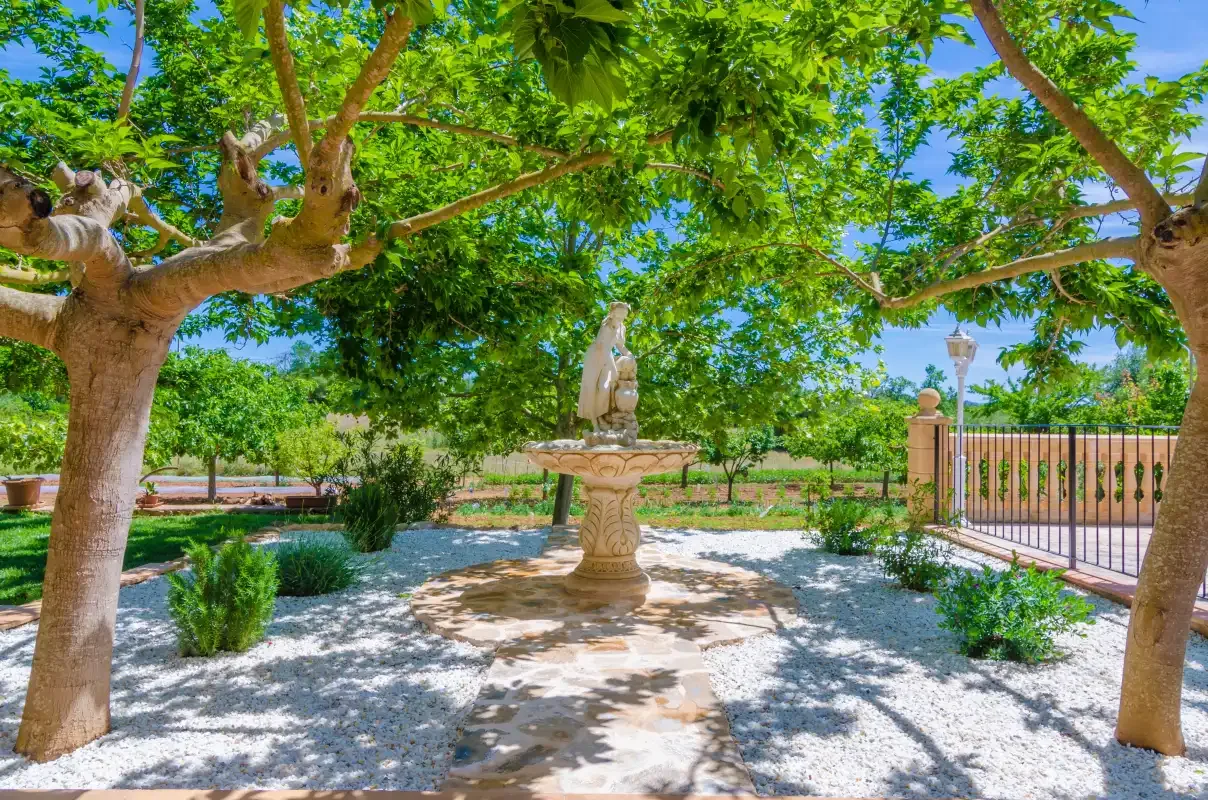 A shaded garden courtyard features a stone fountain beneath leafy trees.