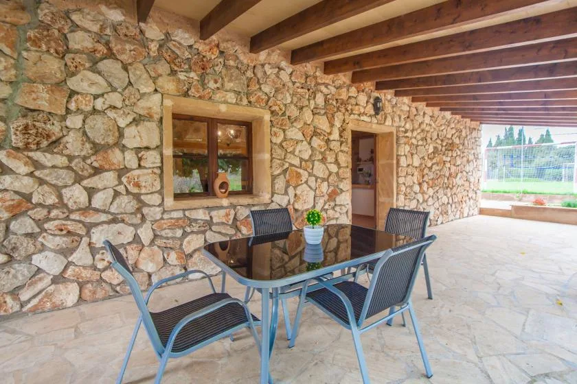A covered stone patio has a glass-top table and outdoor seating.