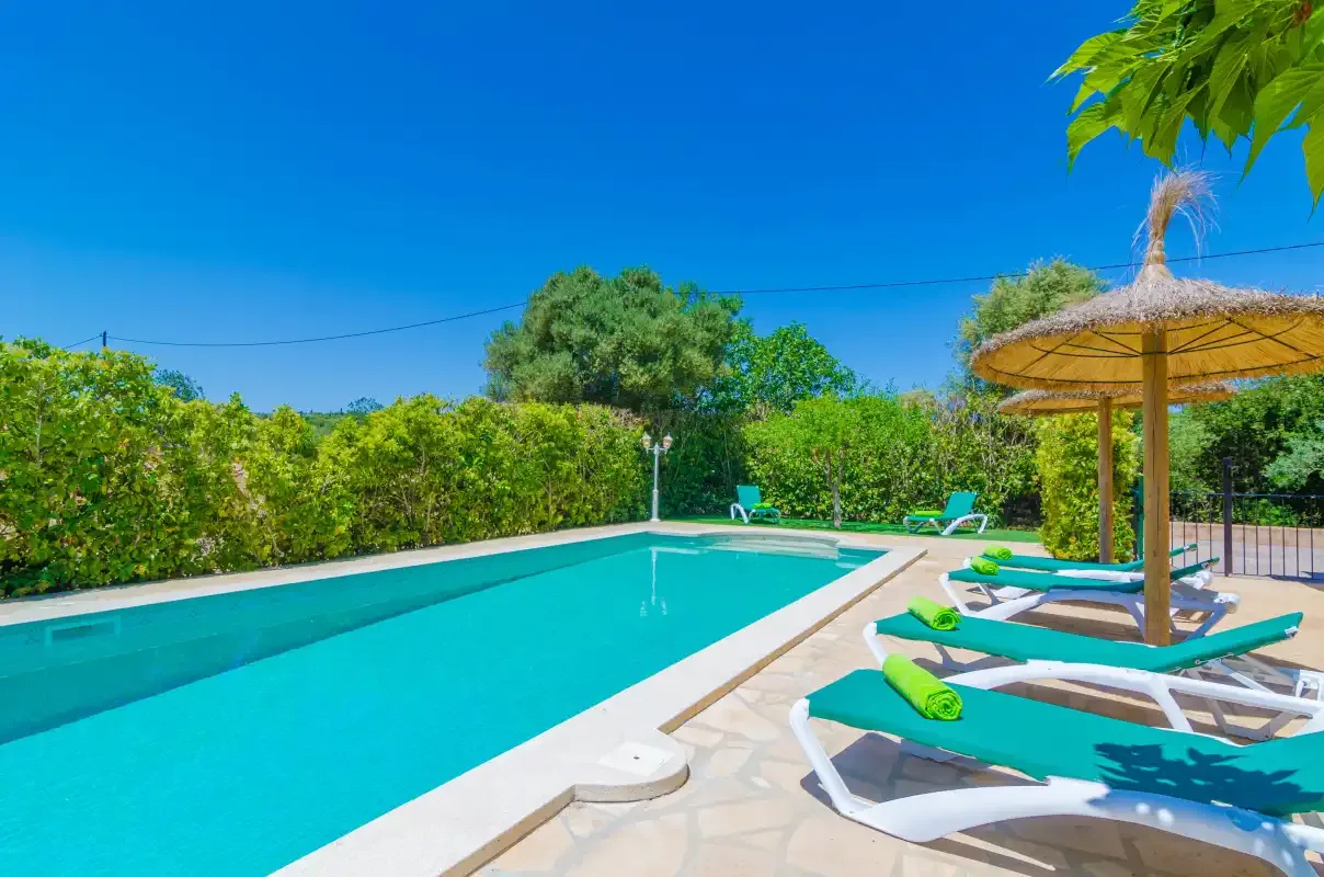 An outdoor swimming pool beside sun loungers and a thatched parasol.