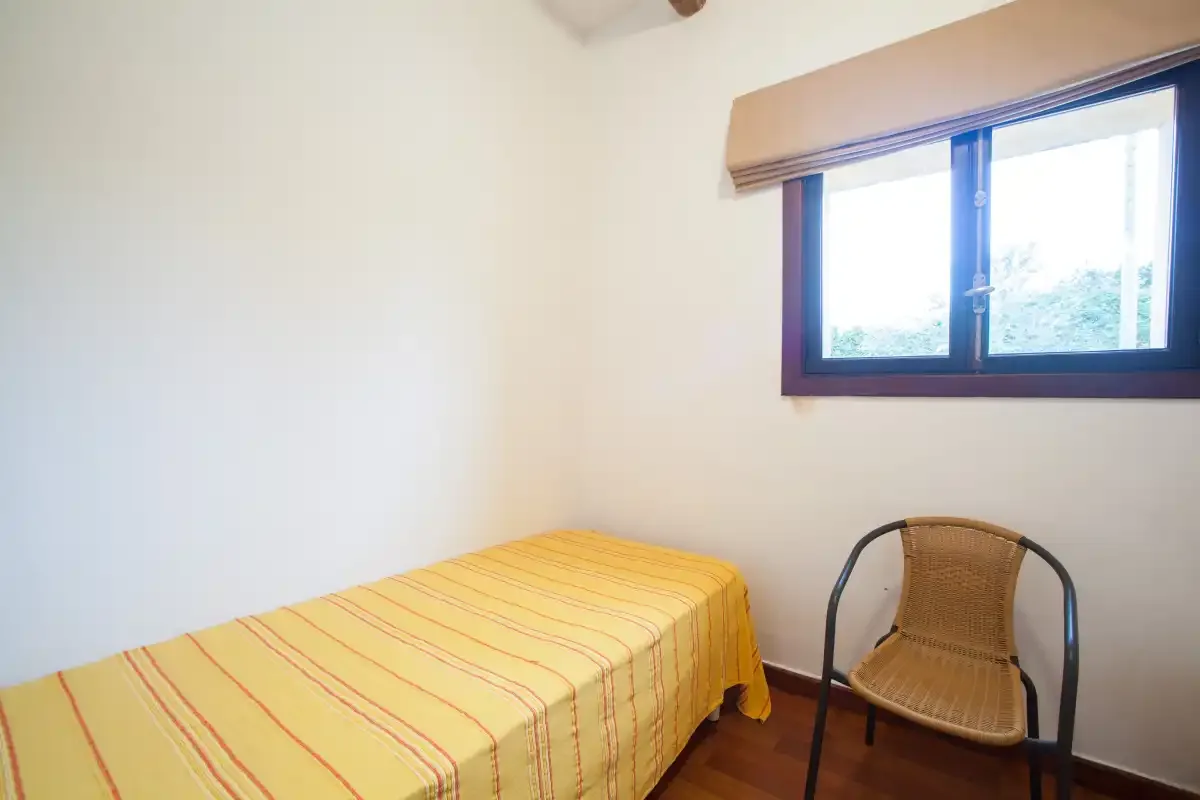 A simple bedroom with a single bed and a chair beside the window.