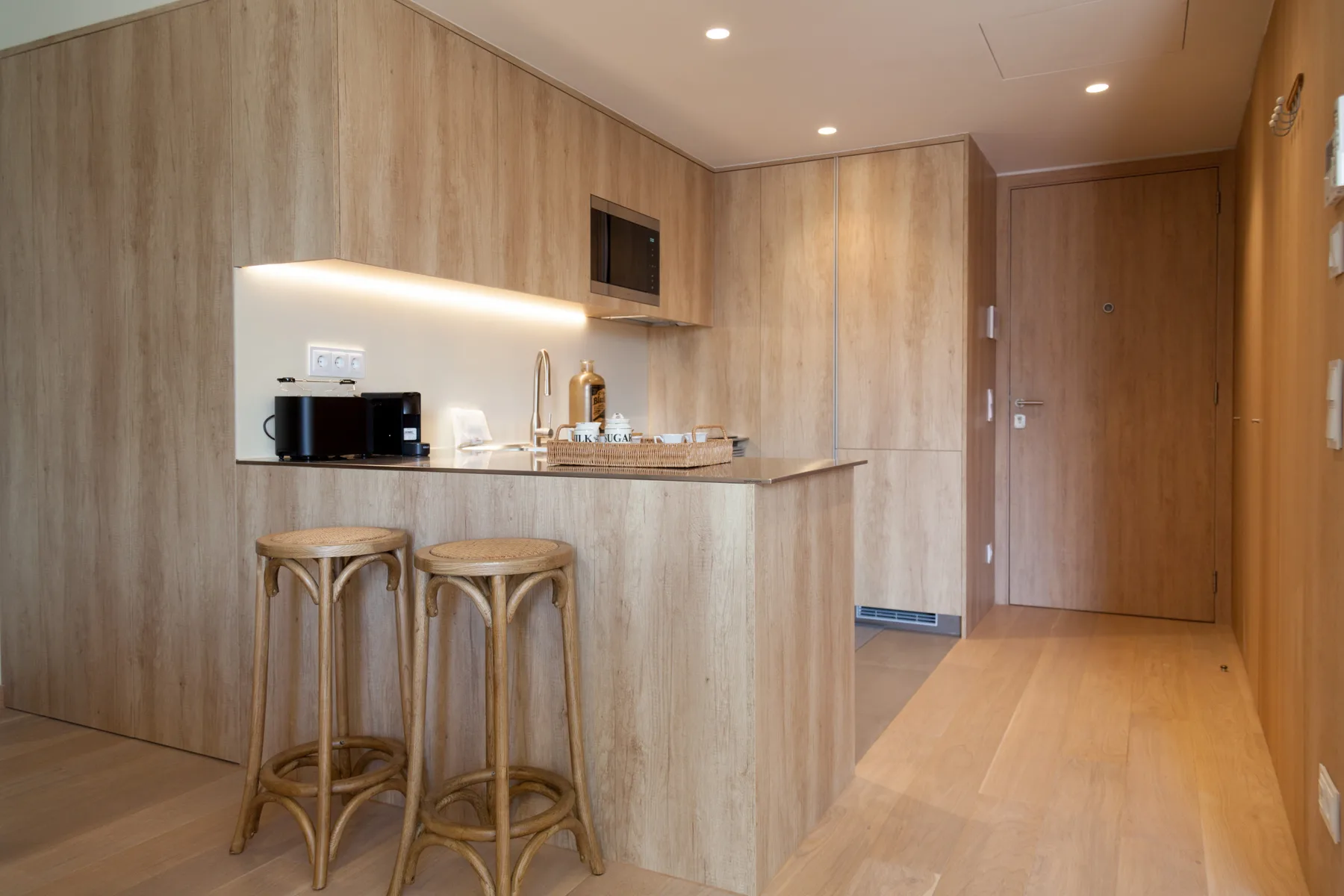 A compact kitchen counter with two stools sits beside a wooden entry door.