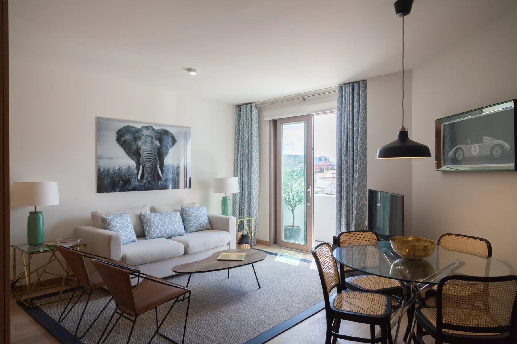 A bright living and dining room with a sofa, glass table, and balcony doors.