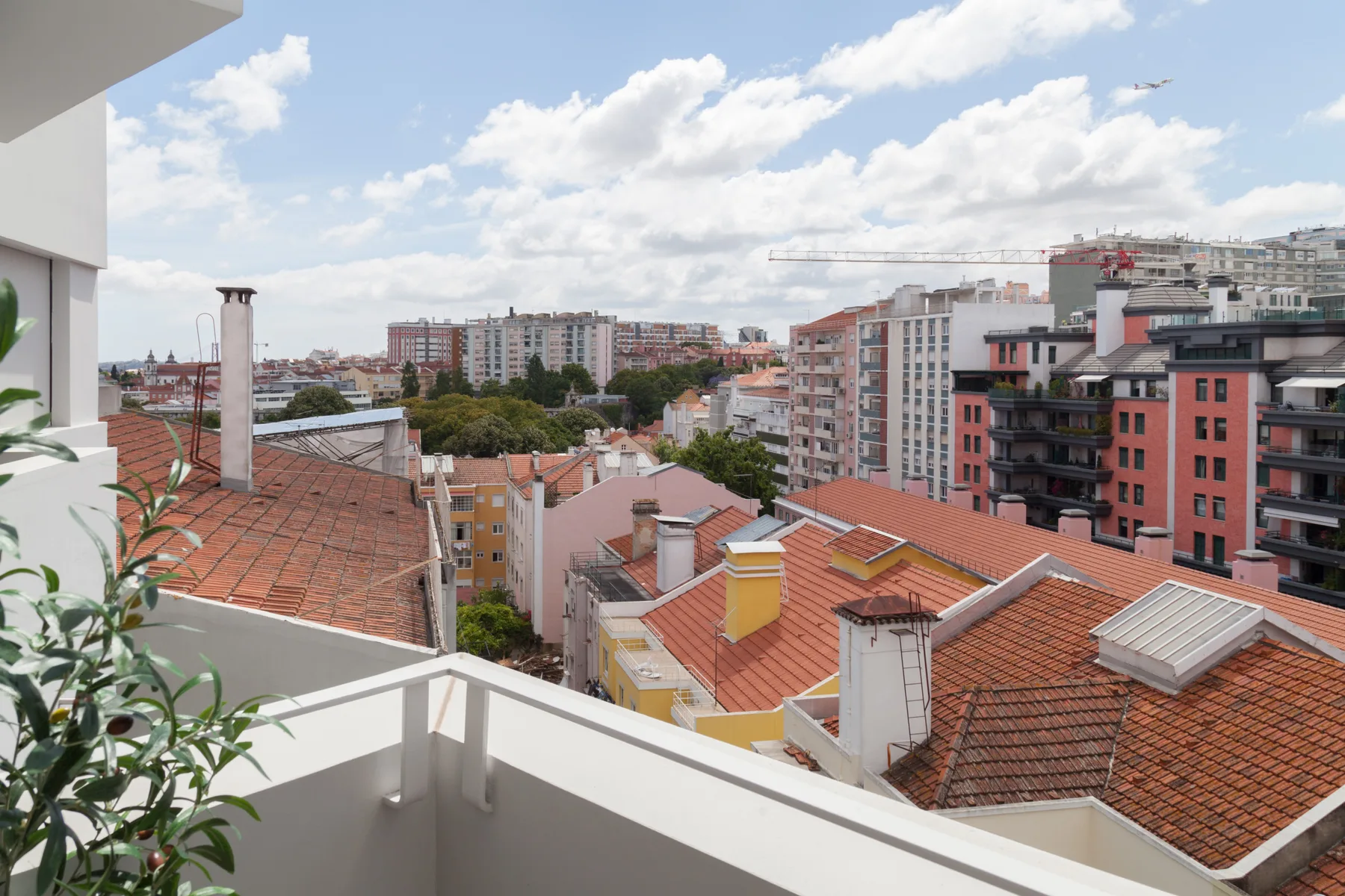 A balcony overlooks red-tiled rooftops and apartment buildings beneath a cloudy sky.