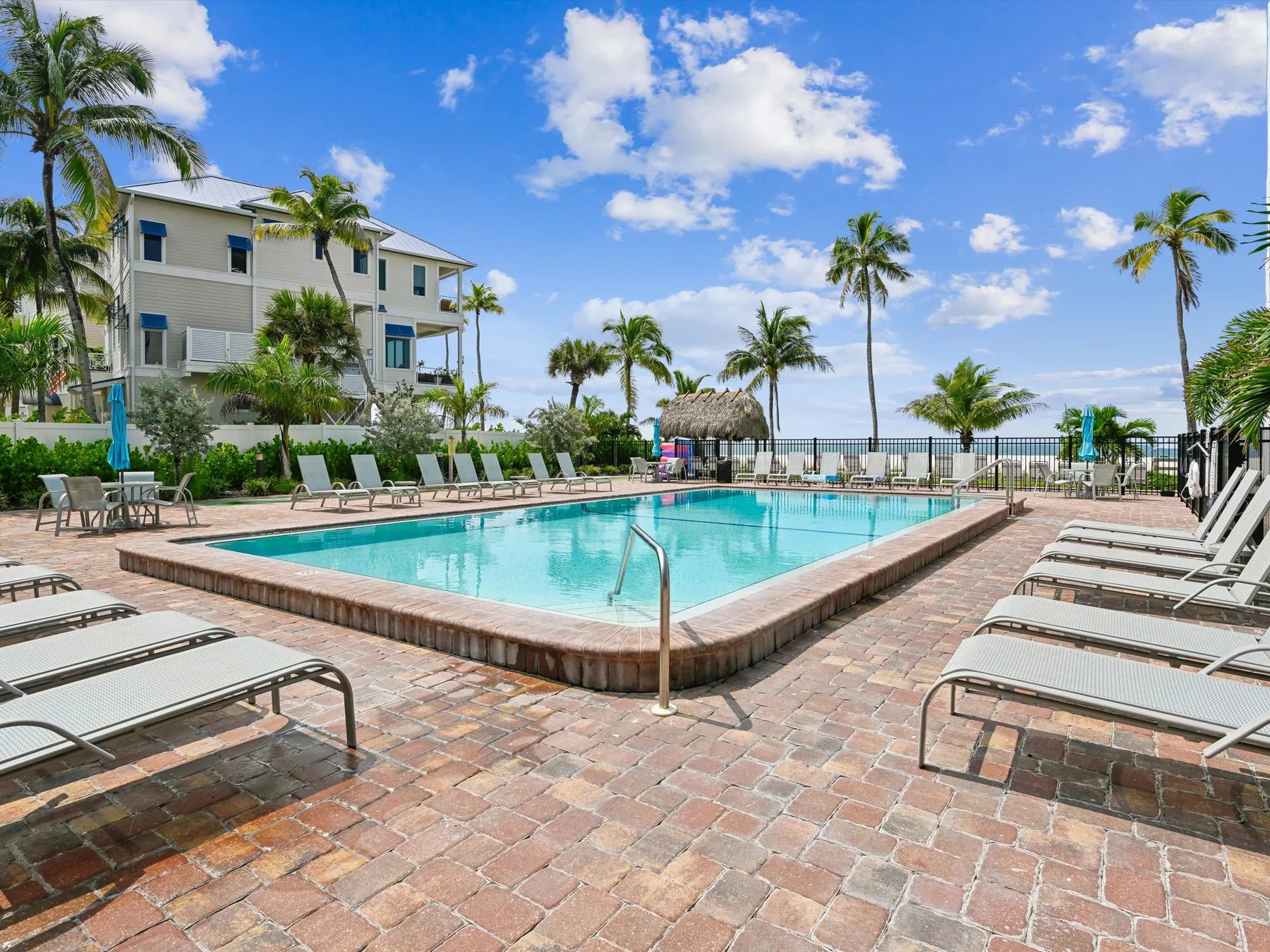 An outdoor swimming pool is surrounded by lounge seating and palm trees.