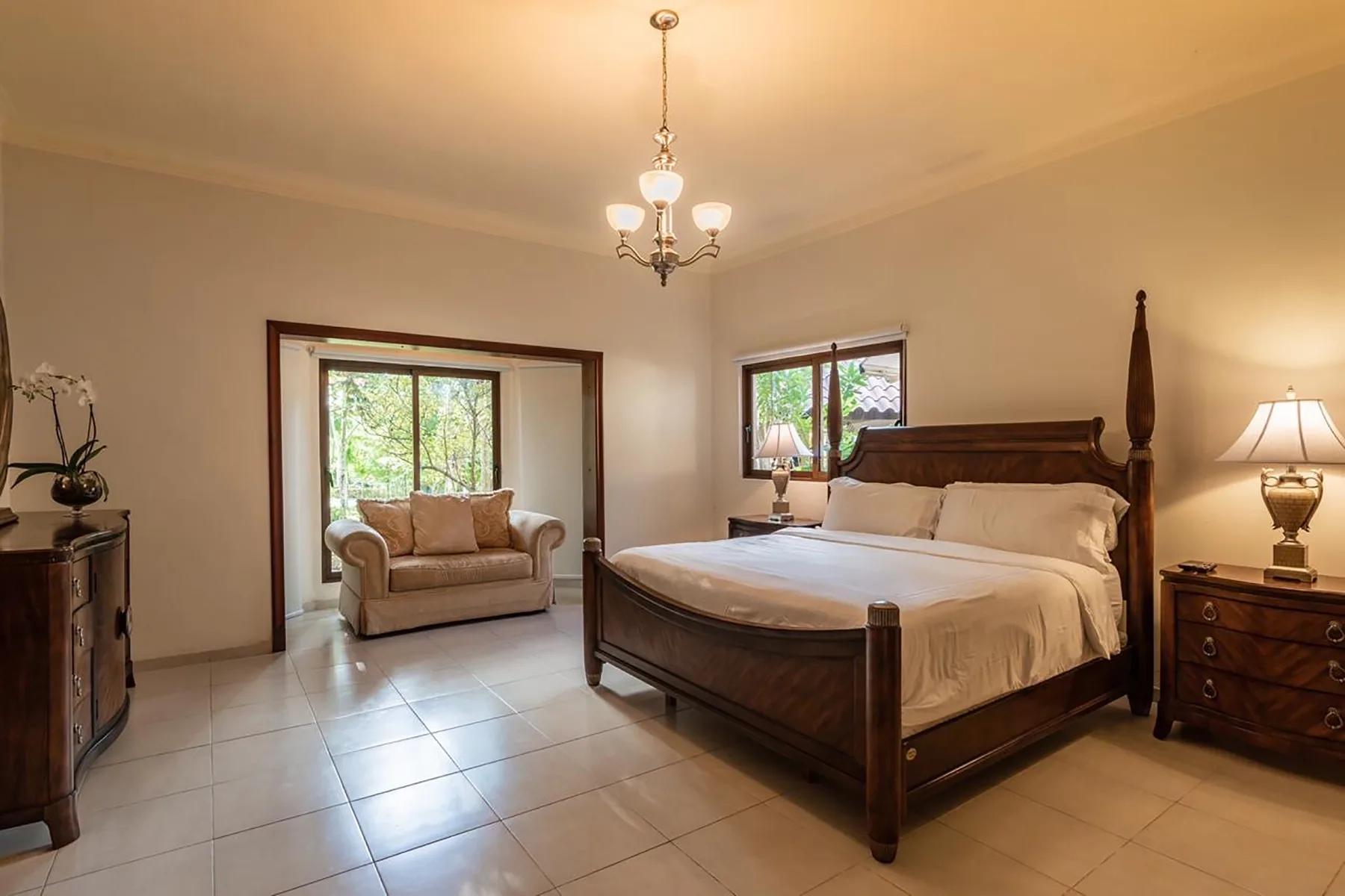 A bedroom with a large bed, bedside tables, and a seating area by the windows.